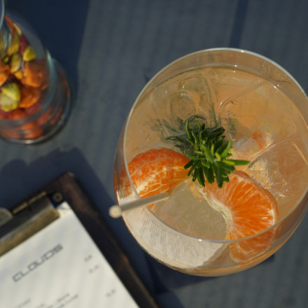 Auf einem Tisch steht ein Zitruscocktail mit Eis und Garnitur neben einer verschwommenen Speisekarte und einem Glas mit gemischten Nüssen.