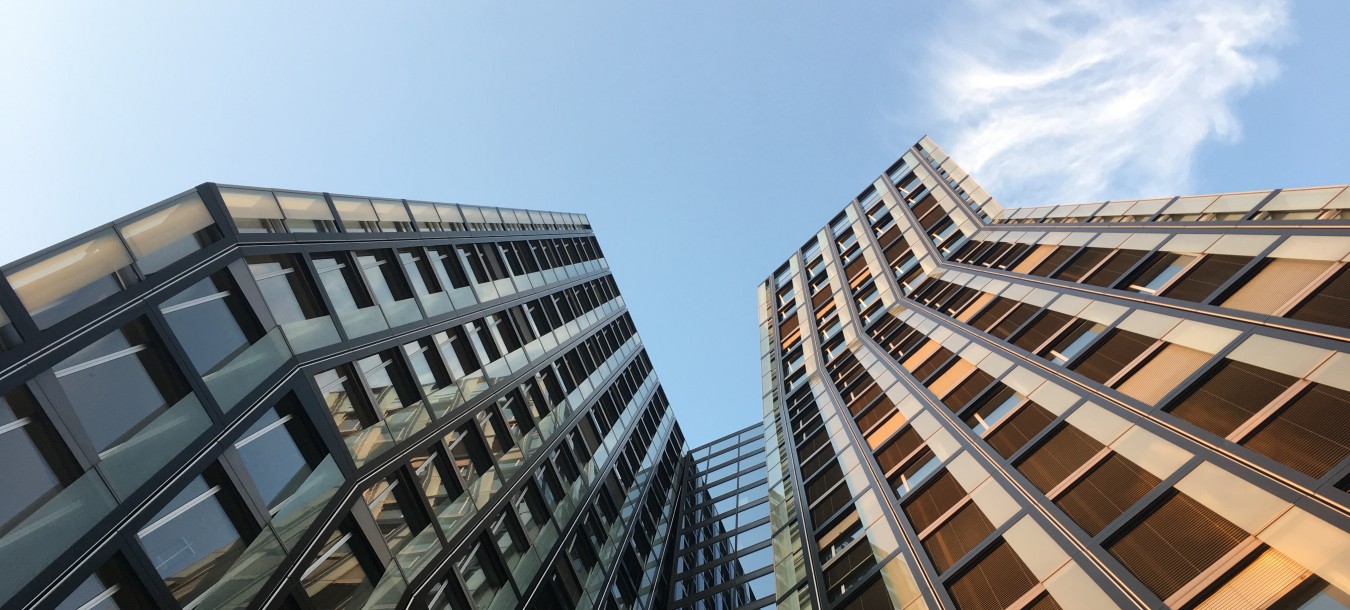 Hohe, moderne Glasgebäude wachsen nach oben und spiegeln den blauen Himmel und eine dünne weiße Wolke wider.